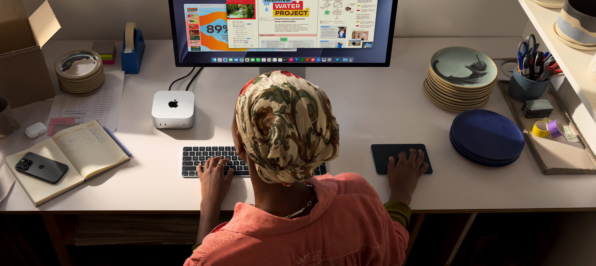 En person sidder ved et skrivebord og skriver med en Mac mini, Studio Display tilsluttet, Magic Keyboard, Magic Trackpad og forskellige ting