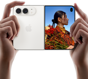 iPhone Duo, zvjezdano bijele boje, drži se dvjema rukama u vodoravnoj orijentaciji, otvoren, lijevi panel prikazuje stražnje dvojne kamere Fusion od 48 MP, desni panel prikazuje osobu koja snima fotografiju na vanjskom zaslonu, objekt fotografije može vidjeti svoje lice dok se fotografija snima koristeći Duo Preview