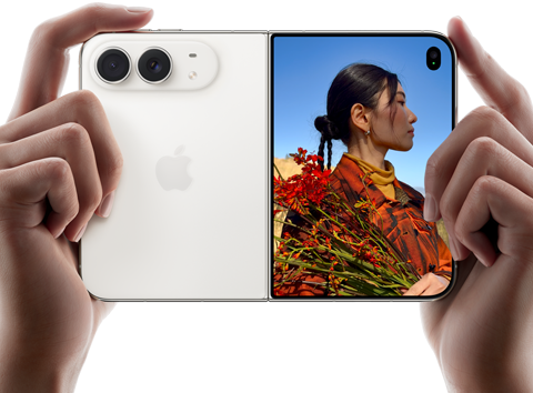 iPhone&nbsp;Duo, zvaigžņu baltā krāsā, tiek turēts divās rokās horizontālā novietojumā, atvērts, kreisajā panelī redzamas 48&nbsp;MP Dual&nbsp;Fusion aizmugurējās kameras, labajā panelī redzams, kā ārējā displejā tiek uzņemta cilvēka bilde, fotografējamais redz savu seju, kamēr tiek uzņemta bilde ar Duo&nbsp;Preview