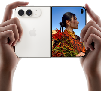 iPhone Duo, Star White color, held by two hands in horizontal orientation, unfolded, left panel shows 48MP Dual Fusion rear cameras, right panel shows person getting their picture taken on outer display, the subject of the photo is able to see their face as their picture is getting taken using Duo Preview