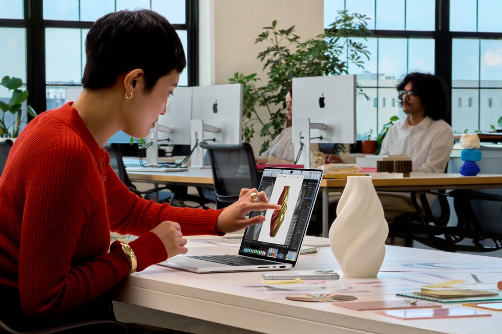 A user seated at a desk in an office environment touches the screen on their MacBook Pro with PROLED XDR Display.