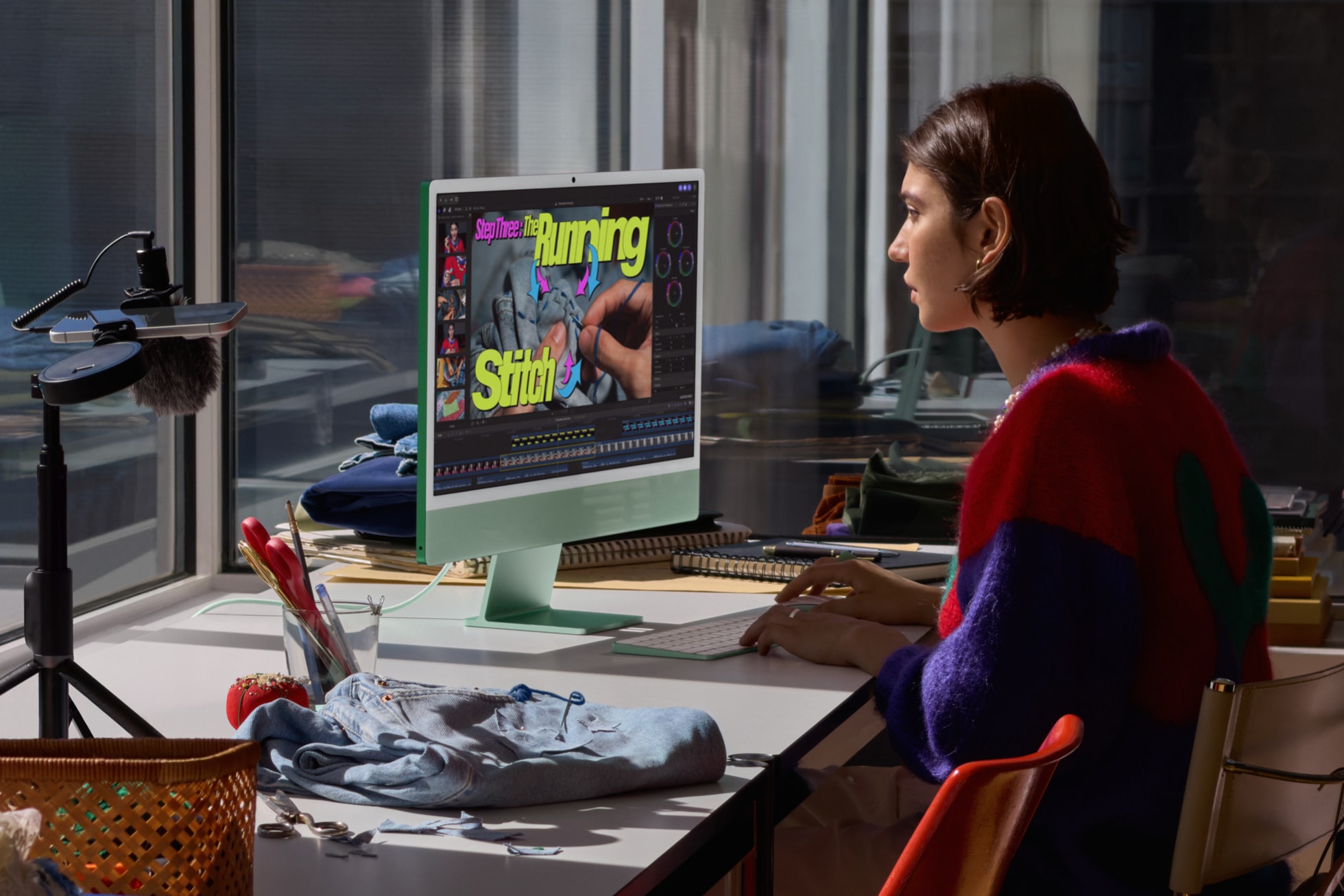 Uma pessoa está sentada em frente ao iMac com M6 na cor verde, ao lado de um projeto de costura, enquanto edita um vídeo.