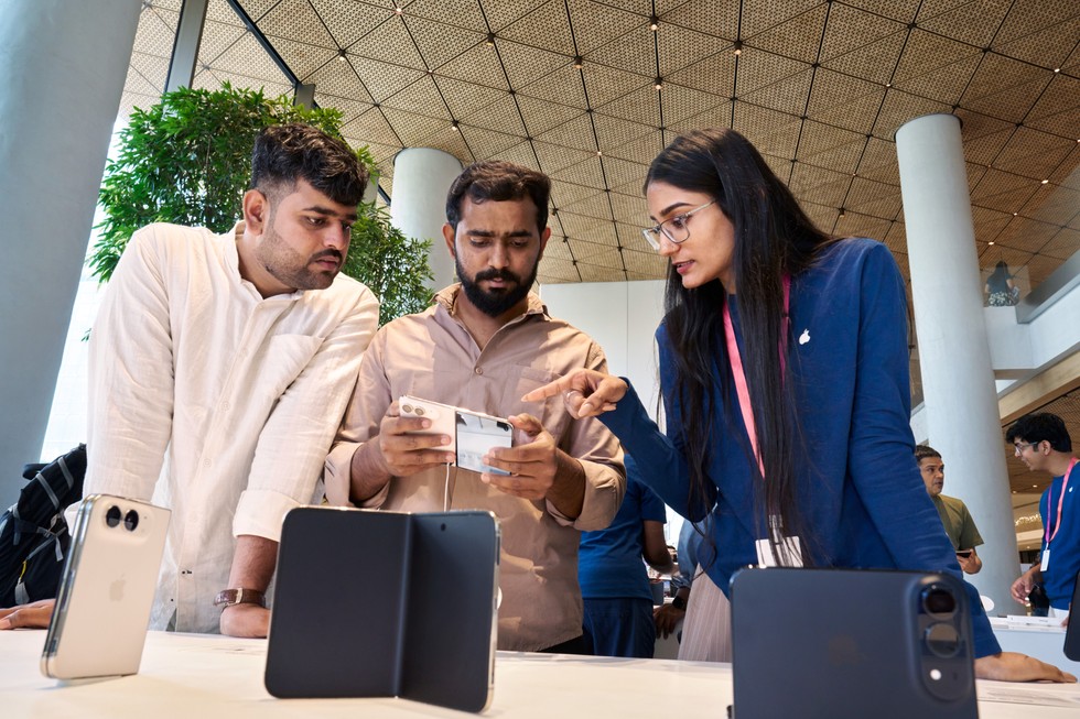 At Apple BKC, an Apple team member assists a customer at the iPhone Duo display table while another person looks on.
