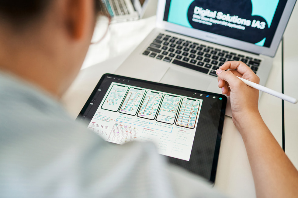 Usando un iPad, un Apple Pencil y una MacBook Air, un estudiante trabaja en el desarrollo de una app.