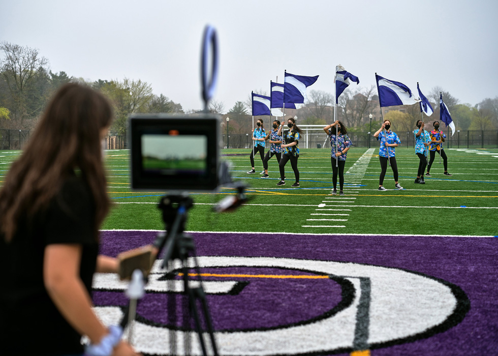 Una estudiante de la preparatoria New Rochelle usa un iPad para grabar a otras estudiantes con banderas en el campo de deportes.