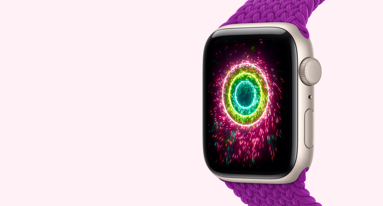 Apple Watch SE 3, boîtier en aluminium lumière stellaire associé à un Bracelet Boucle unique tressée magenta, sur l’écran, les anneaux Activité s’illuminent tels des étincelles qui forment des cercles concentriques roses, vert citron et bleu clair.