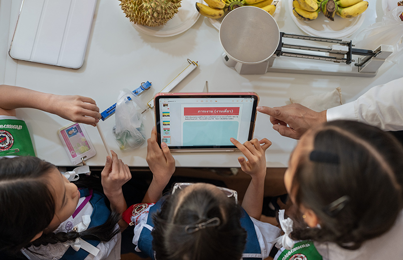 Three elementary students gather around iPad to collaborate on a presentation for a science project.