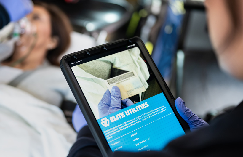 App Elite Utilities aberta no iPad com um paramédico a digitalizar a carta de condução de um doente, que está deitado numa maca
