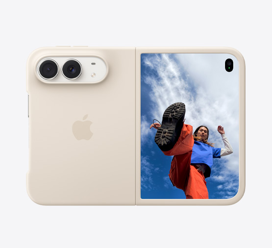Stjernehvid iPhone Duo med sandfarvet silikone-cover, vandret position, helt åbne, Fusion-dobbeltkameraer øverst til venstre, coveret dækker bagsiden og yderkanten af yderskærmen, højre side viser ydreskærmen med et billede af en person, der står under en skyfri blå himmel