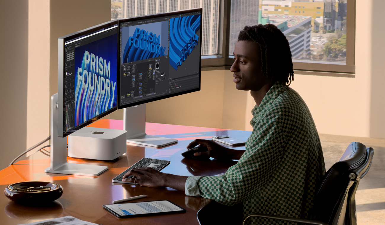 Una persona sentada en un escritorio con un Mac Studio ubicado entre dos monitores Studio Display, las pantallas muestran varios proyectos en curso en apps de animación y edición