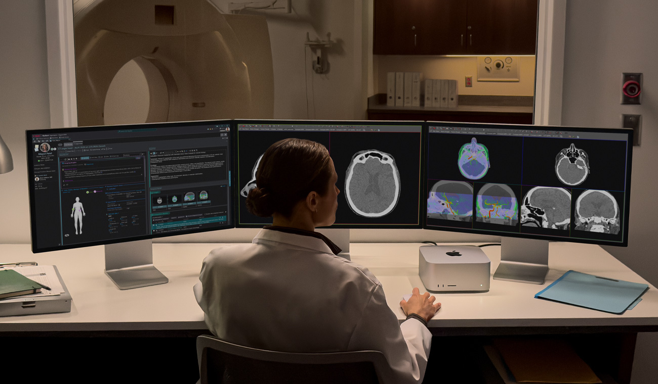 Una persona sentada en un escritorio con tres monitores Studio Display uno al lado del otro, un Mac Studio sobre el escritorio, todas las pantallas muestran aplicaciones de imágenes médicas