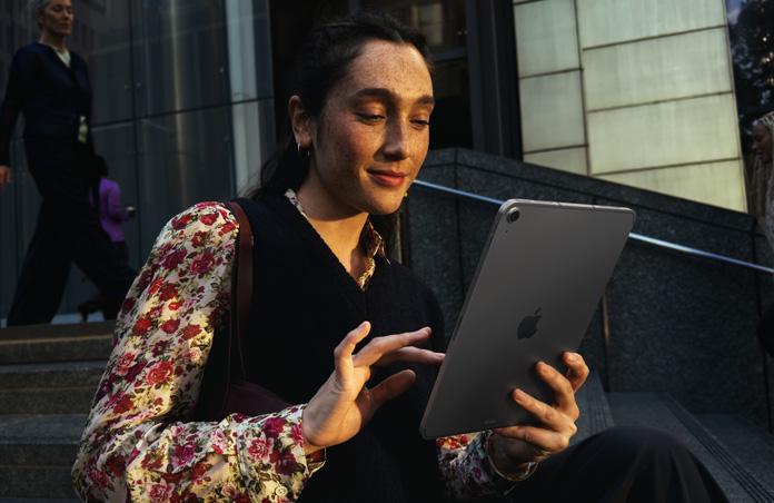 Henkilö istuu portailla suuren rakennuksen edustalla ja käyttää tähtiharmaata 11 tuuman iPad Airia, jonka wifi-yhteys säilyy saumattomasti verkkoa vaihdettaessa