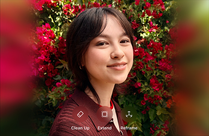 Foto di una persona sorridente con i capelli castani che indossa un maglione marrone ed è circondata da fiori rossi; dimostrazione del fotoritocco AI con le opzioni Ripulisci, Estendi e Reinquadra mostrate sulla foto